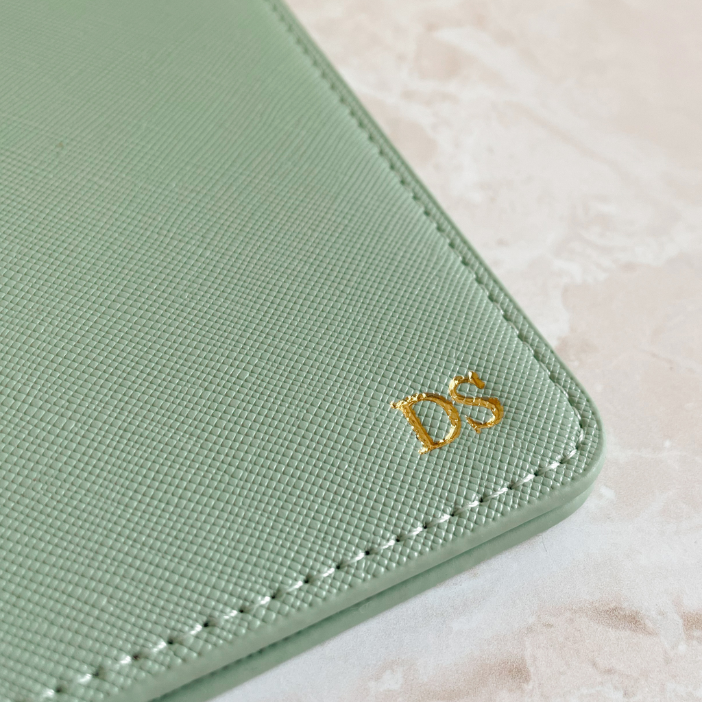 Detalle iniciales grabadas en caliente sobre funda pasaporte cuero verde sage