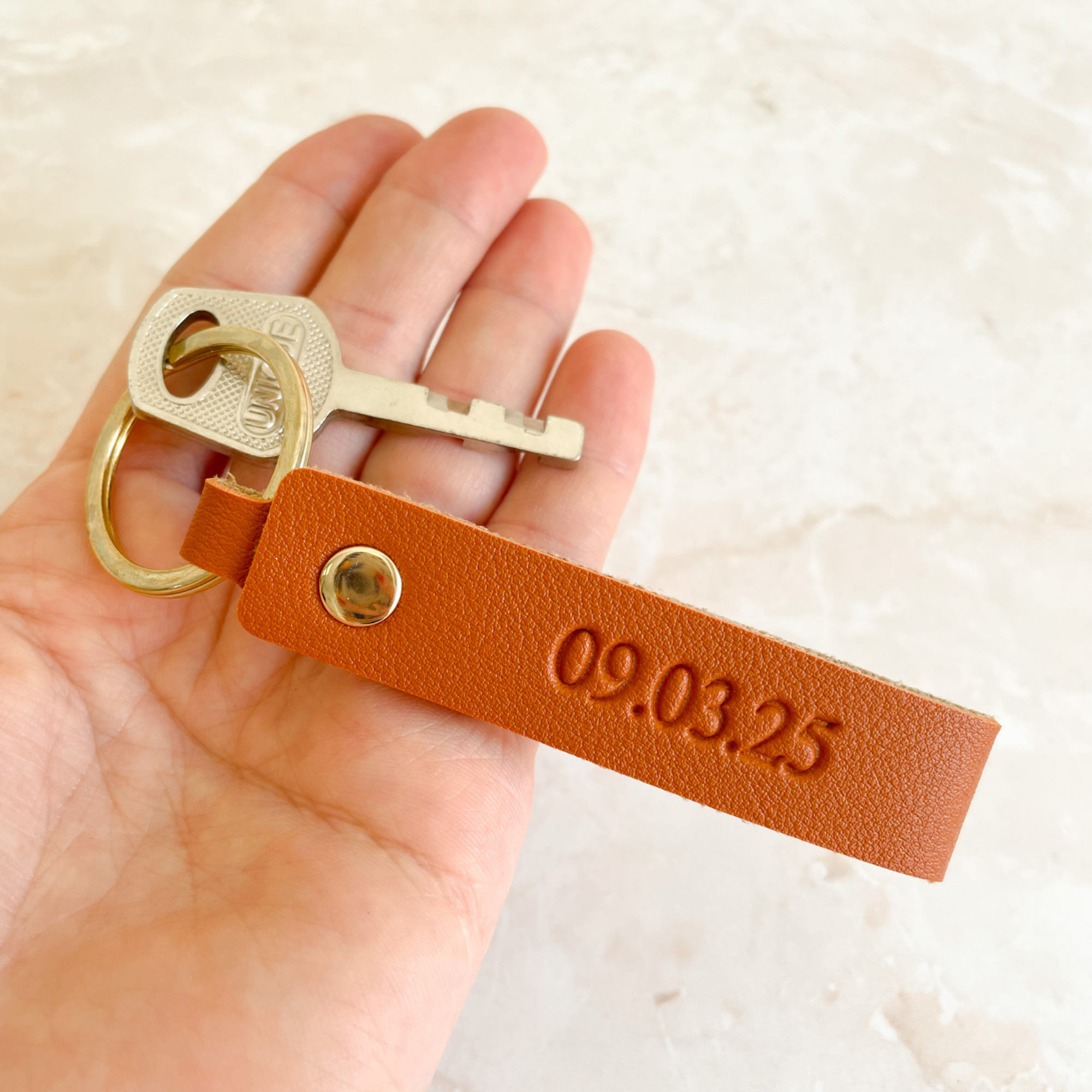 Llavero de cuero personalizado con fecha grabada sostenido en mano - detalle acabado camel