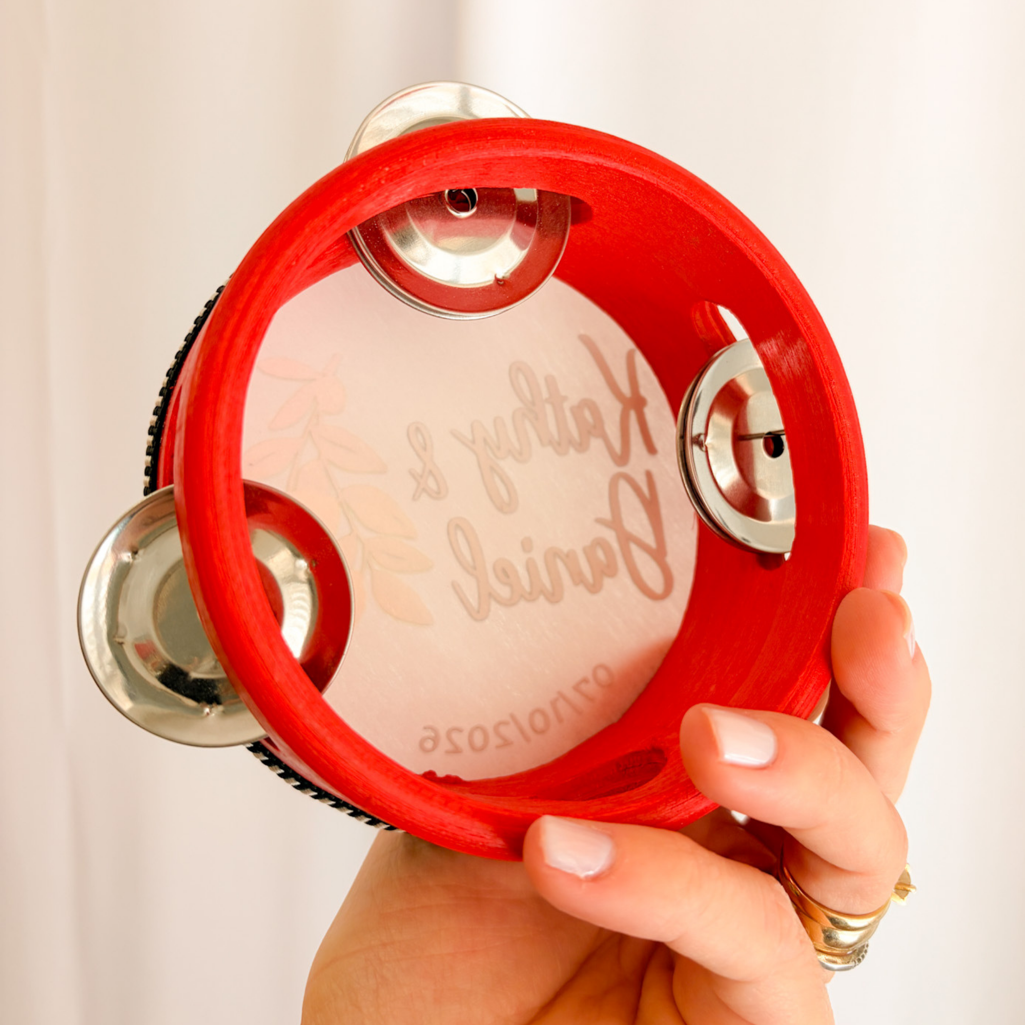 Detalle de pandereta personalizada para boda en rojo con nombres grabados sostenida en mano